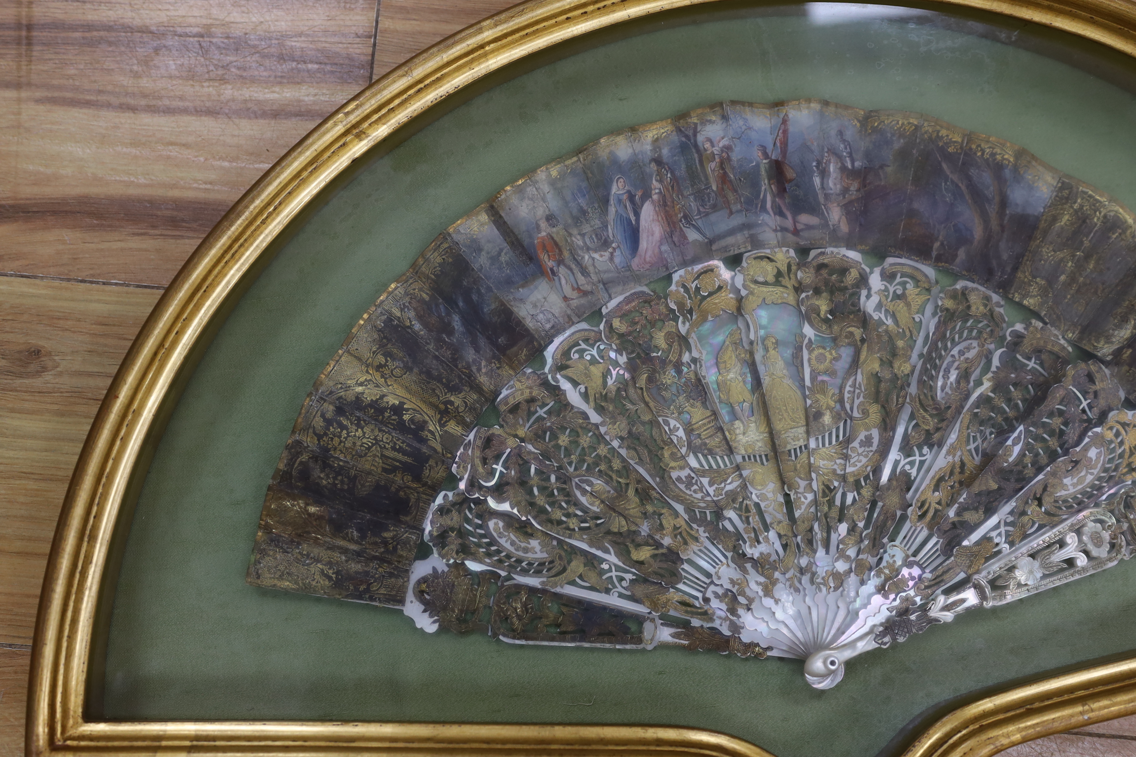 A cased early 19th century French painted paper leaf fan with gilt and mother of pearl sticks, fan 24cm high